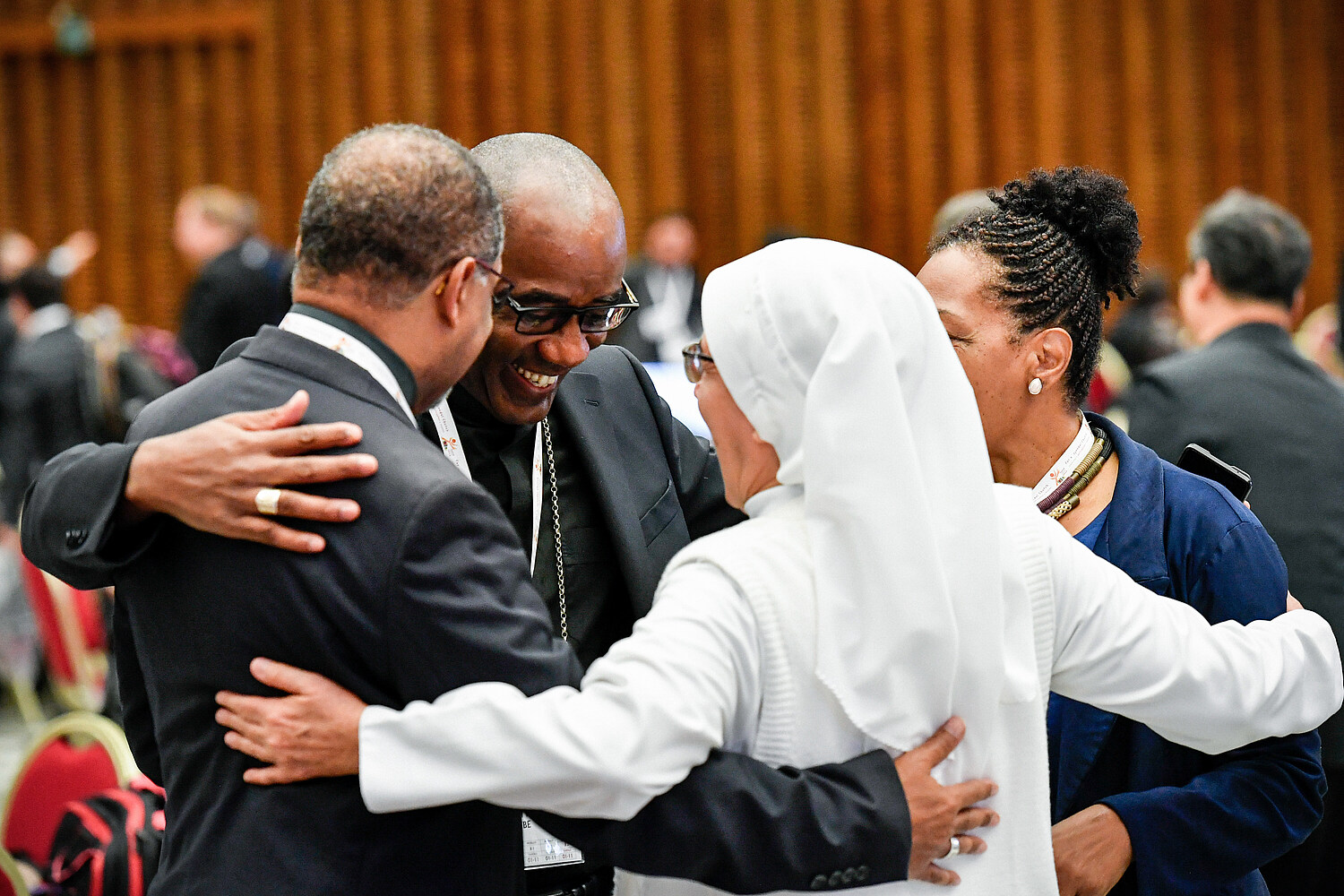 Teilnehmer umarmen sich bei der Weltsynode / Copyright 2023, KNA GmbH, www.kna.de, All Rights Reserved, Vatican Media Zwei Teilnehmerinnen und zwei Teilnehmer, darunter eine Ordensschwester, umarmen sich während der Weltsynode am 23. Oktober 2023 im Vatikan.
